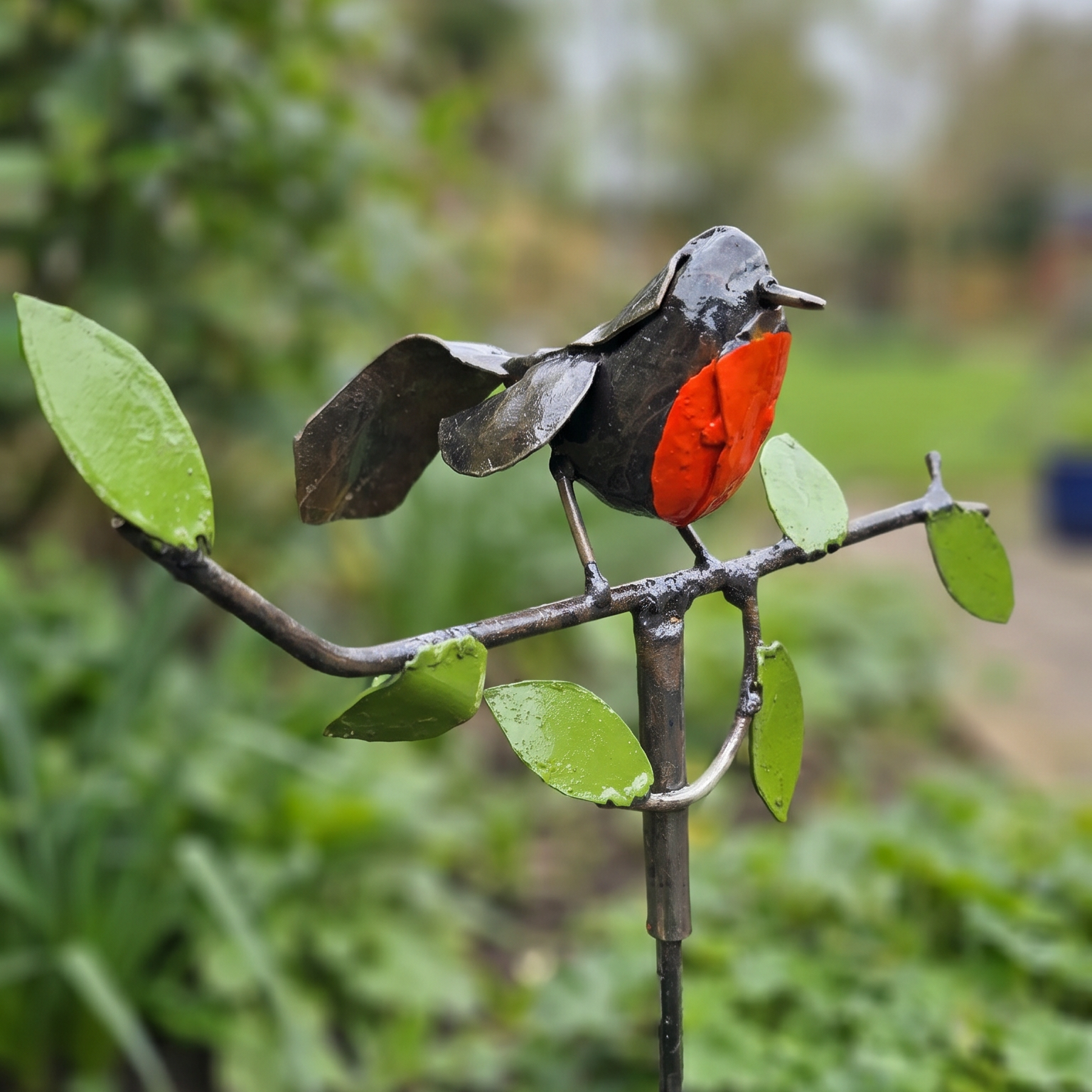 Metal sculpture of a bird perched on a branch with leaves in a garden setting
