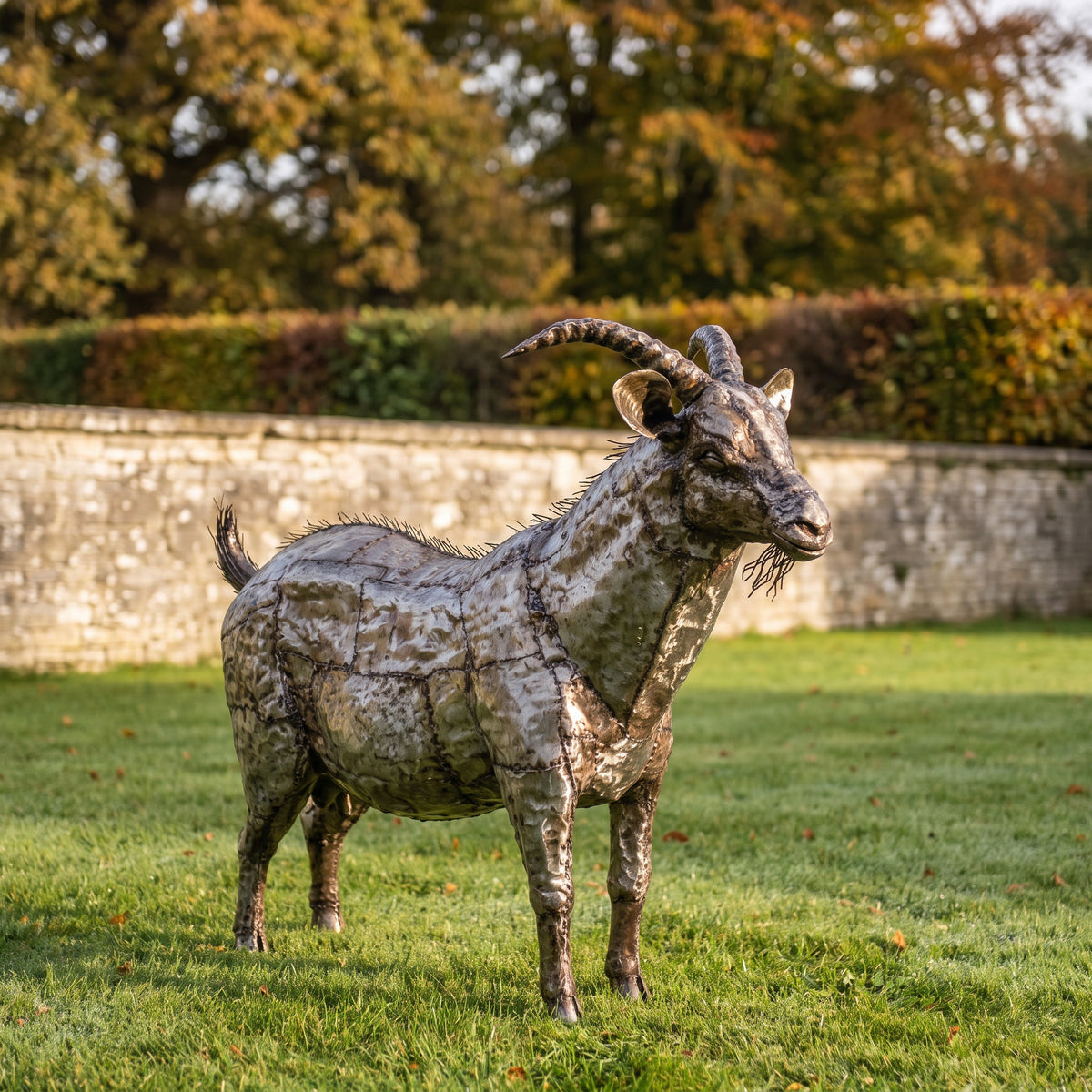 Goat metal sculpture on a lawn beside an autumn garden wall