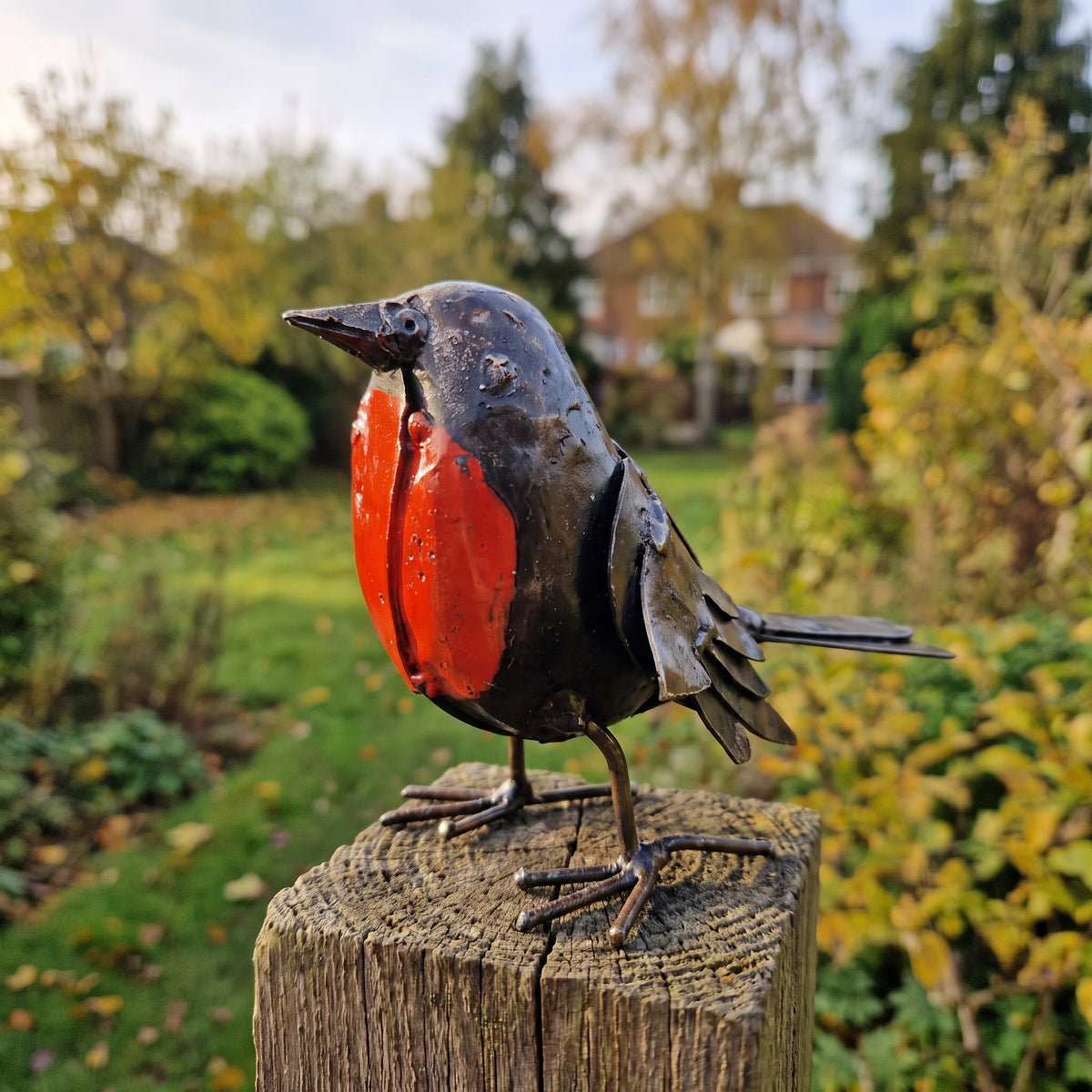 Painted Robin metal sculpture perched on a stump in an autumn garden
